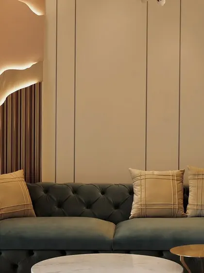 A closer look at the living room with the custom illuminated wall feature. The deep green, tufted velvet sofa provides a rich textural contrast to the smooth, neutral walls and the warm glow of the integrated lighting.