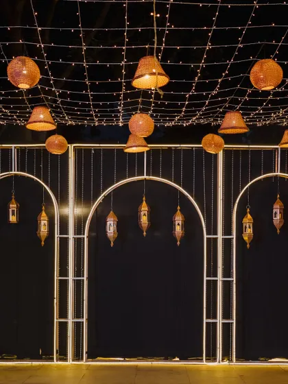 A modern and chic Sangeet stage with a black backdrop, illuminated by arched frames and hanging Moroccan-style lanterns. The design is perfect for a glamorous evening of music and dance.