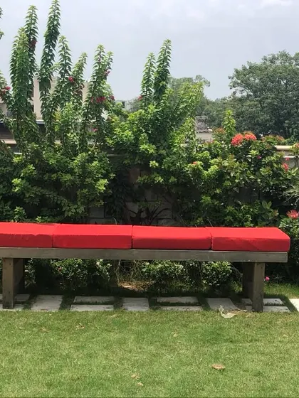 A terrace garden with a cot is always so inviting. This simple wooden bench with a red cushion, set against a backdrop of tall planters and shrubs, is a perfect spot to enjoy the morning sun.