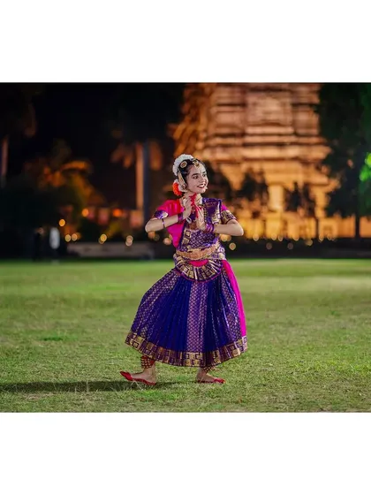 A dancer performs a Bharatanatyam piece on a lawn at dusk, with an illuminated temple in the background. This shot demonstrates my use of ambient and artificial light to create a serene and visually rich performance photograph.