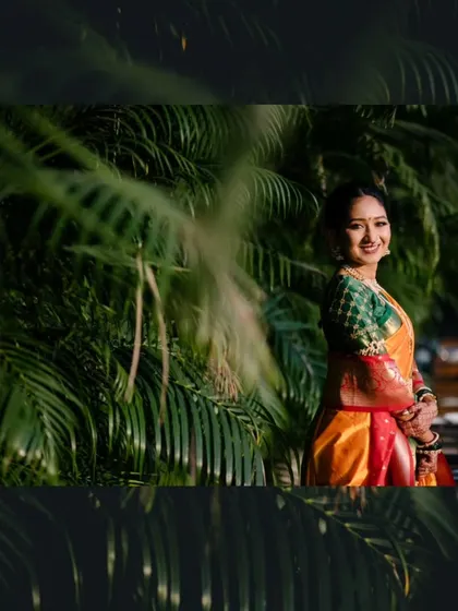 A beautiful bridal portrait of the bride smiling, framed by lush green foliage that makes her colorful saree pop.