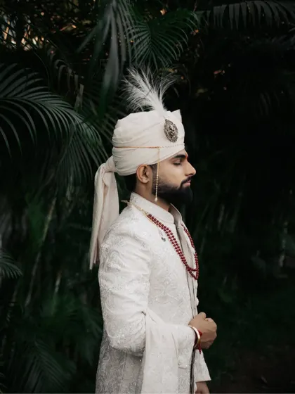 A solo portrait of the groom in his elegant white sherwani and feathered turban.