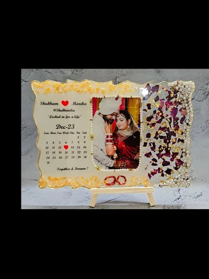 A still image of the finished wedding varmala preservation frame, complete with a calendar, photo, and preserved petals. It comes with a wooden stand for easy display.