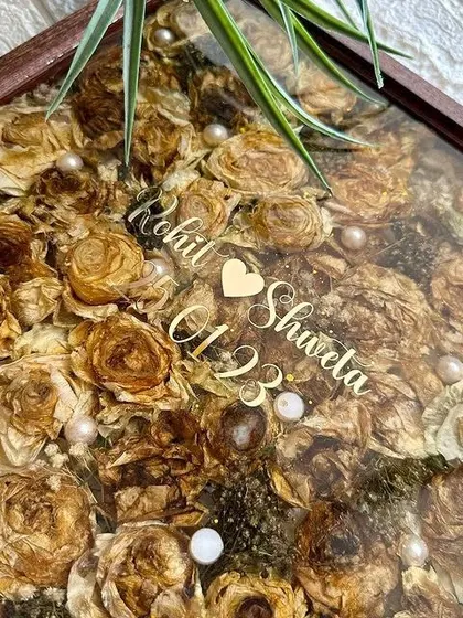 A top-down view of the packed floral keepsake, showing the texture and depth of the preserved flowers. The personalized acrylic text adds a modern touch to the rustic frame.