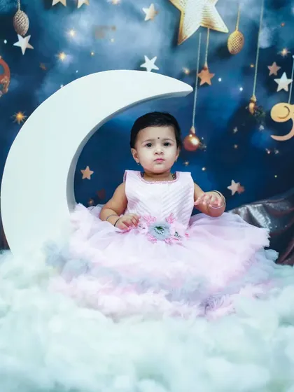 A princess on the moon. This dreamy indoor setup features a large moon prop, fluffy clouds, and a starry night backdrop for a magical portrait.