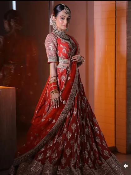 A full-length shot of a bride in a red lehenga, showcasing the elegant silhouette and the detailed embroidery that makes it a timeless choice.