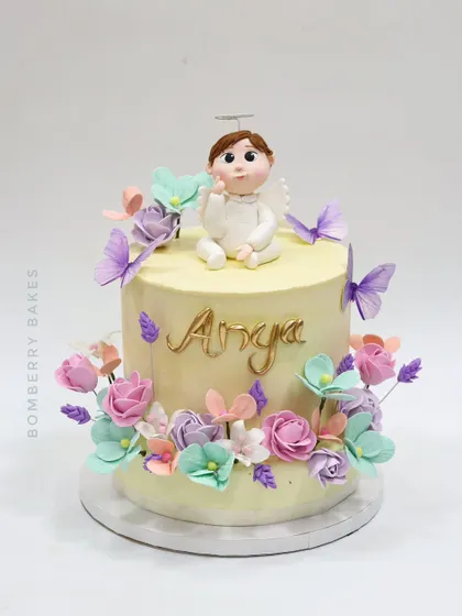 A lovely baptism cake for little Anya, featuring a sweet angel figurine, pastel flowers, and delicate butterflies.