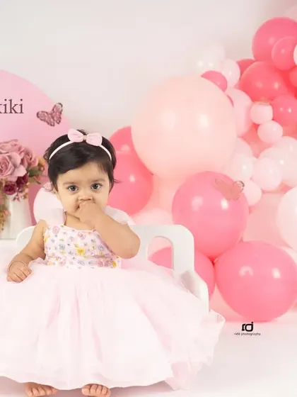 A shy moment during her butterfly-themed first birthday shoot. The pink and white balloons create a beautiful, soft background.