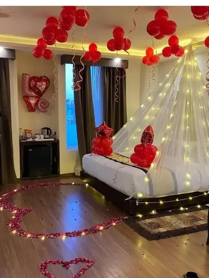 I created this romantic room setting with red balloons, a heart made of artificial rose petals on the floor, and a bed canopy illuminated with warm fairy lights. It's a classic setup for an anniversary or special surprise.