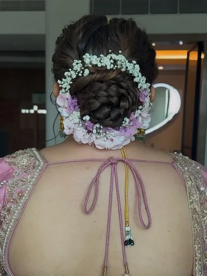A lovely bridal bun created with a mix of baby's breath and light purple flowers. This style is perfect for a daytime wedding or a bride looking for a soft, romantic floral arrangement in her hair.