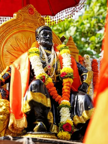 A close-up of the beautifully adorned statue of Chhatrapati Shivaji Maharaj. The detail in the garlands and the regal posture of the statue are the central focus of this shot.