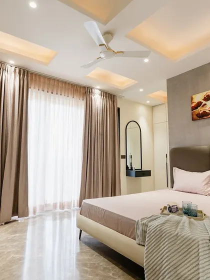 This spacious bedroom uses a neutral palette and floor-to-ceiling windows to create an airy feel. The dark, textured headboard and abstract art add a touch of drama.