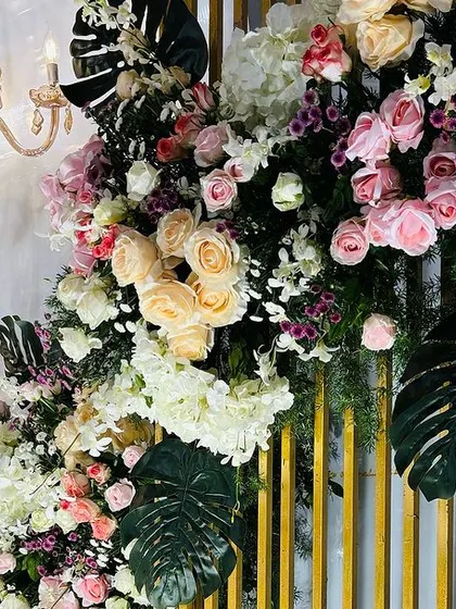 A detailed shot of a floral arrangement, showing the interplay of light from a chandelier with the textures of flowers and monstera leaves.