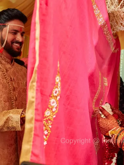 A creative shot taken during the Antarpat ritual, capturing the smiles of the bride and groom as they see each other for the first time through the sheer cloth.