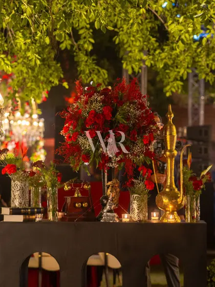 A detail shot of a console table, styled for the Sufi night. A large arrangement of red roses is complemented by antique props like a brass surahi and a vintage telephone, adding to the old-world charm.
