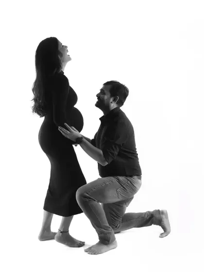 A joyful and candid black and white photo. The mom-to-be is laughing happily as her partner kneels before her, a moment of pure, unscripted happiness.