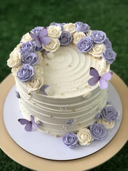 A beautiful white cake with a cascade of purple and white buttercream roses and delicate edible butterflies.