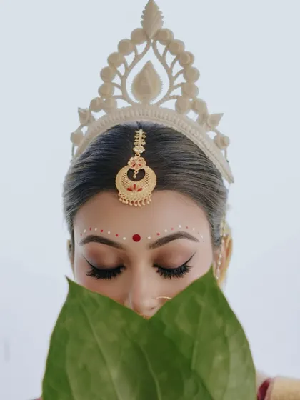 A close-up on the eyes. The 'topor' and the betel leaves frame her face, drawing all attention to her expressive, kohl-lined eyes.