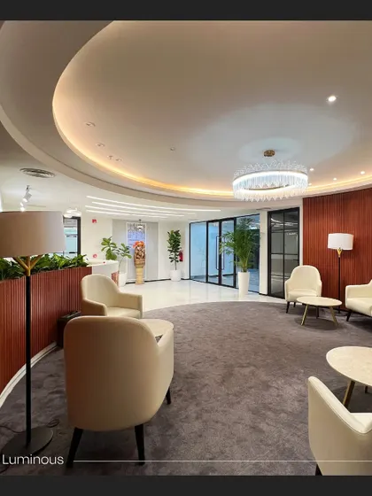 The luminous waiting lounge at the Rays Power office, featuring a circular layout with plush armchairs and soft, recessed ceiling lights. The warm wood paneling and ample space create a comfortable and sophisticated area for visitors.