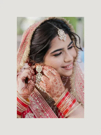 A candid moment of the bride adjusting her earring, her hands adorned with beautiful mehndi. We love capturing these small, natural gestures that happen while getting ready.