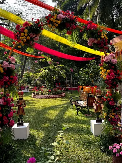 The entrance to a garden Mehendi, with colorful fabric drapes overhead and floral arrangements creating a festive pathway.