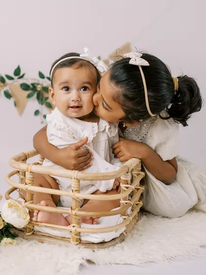 A sweet moment between sisters. The older sister gives her baby sister a gentle kiss during a half-birthday celebration.