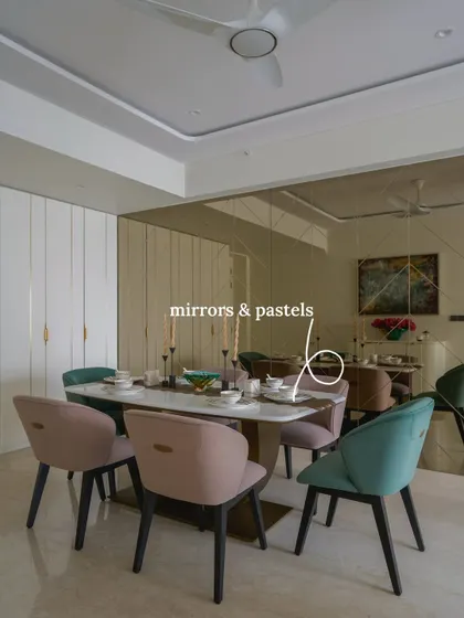 A dining area where mirrors and pastels create a bright, playful atmosphere. The marble-top dining table is set against a tinted mirror-paneled wall that amplifies light, with pastel green and pink chairs adding a pop of color.