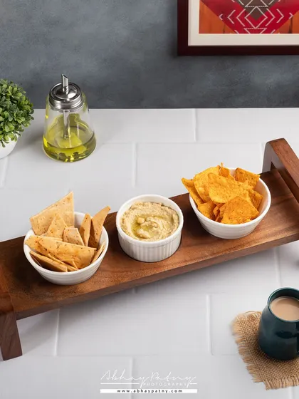 A wooden serving platter styled with snacks and coffee. This lifestyle approach helps sell not just the product, but the experience of using it to entertain guests or enjoy a quiet evening.