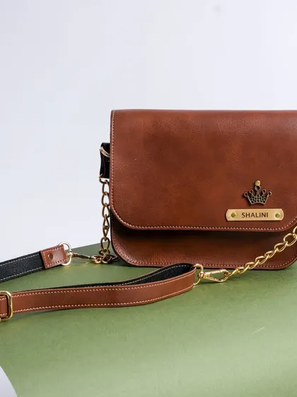A detailed look at the tan NEXON sling bag, customized with a name and a crown charm. It comes with an adjustable premium chain strap.