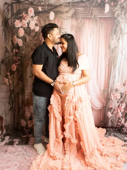 A romantic couple's portrait with a heart-shaped hand gesture on the bump. The floral background adds a touch of fairytale magic.