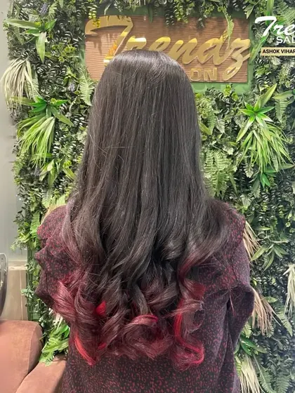A pop of color can make all the difference. Here, we added vibrant red tips to dark hair for a bold and playful look, finished with soft curls.