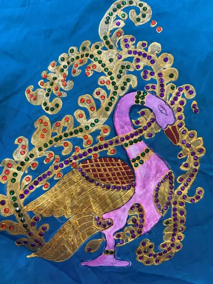 A Thanjavur-style peacock painting on blue fabric, adorned with glittering gold foil and colorful beads. We provide all materials and teach these techniques in our academy.