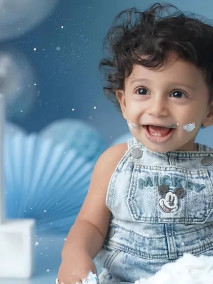 A close-up portrait capturing the infectious, frosting-filled smile of a baby boy during his first birthday cake smash.