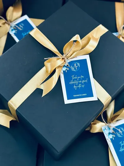 The final look of a perfectly wrapped wedding favor box, tied with a gold ribbon and a custom tag.