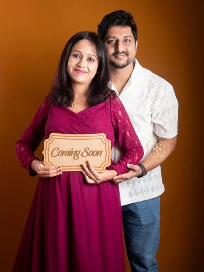 A happy couple posing with a "Coming Soon" sign in our studio. The mom-to-be is wearing a lovely magenta gown.