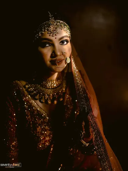 A bride's face is illuminated in the dark, her traditional jewelry and features highlighted in a play of light and shadow. A powerful and dramatic portrait.
