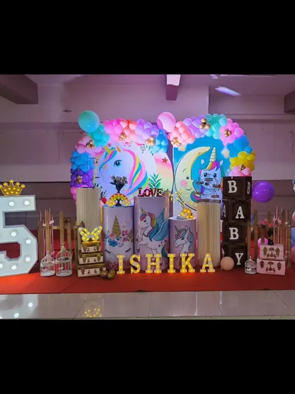 Our unicorn theme is pure magic. This setup for Ishika's birthday features pastel unicorn illustrations on pedestals, a rainbow balloon arch, and light-up letters for an enchanting party.