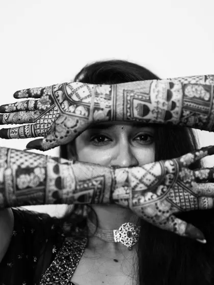 An intimate black and white portrait, with the bride's eyes peeking through her mehendi-covered hands.