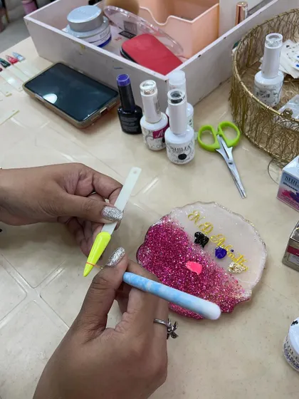 A close-up of a trainer demonstrating a nail art technique using glitter and other embellishments.