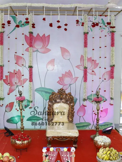 A lovely baby shower setup with a printed lotus backdrop and hanging floral strings. The traditional brass lamps and bowls of fruit complete this serene and beautiful arrangement.