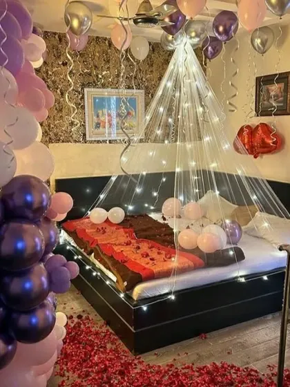 The bed area of the romantic setup, with a floor covered in rose petals and a canopy of lights.