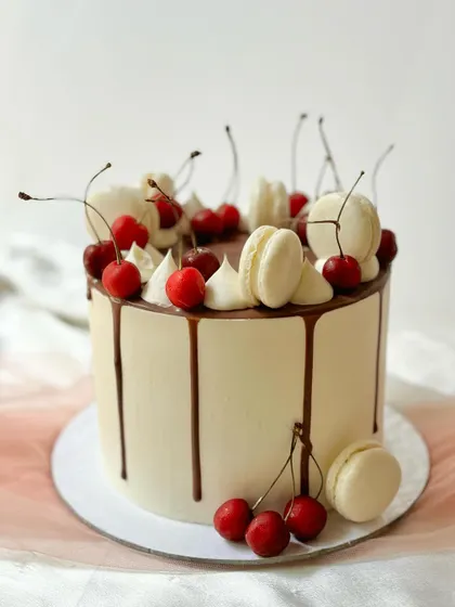A side view of the cherry, chocolate, and macaron drip cake, highlighting the perfect drip and arrangement of toppings.