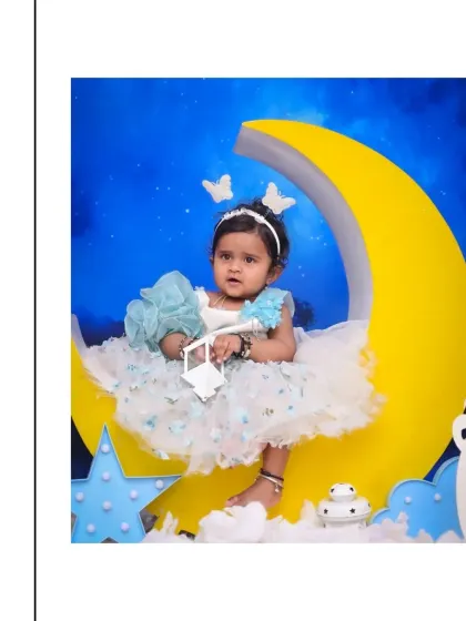 A full-length portrait of a baby girl in a lovely blue and white dress, perched on a yellow moon prop. The butterfly headband adds a touch of whimsy to this dreamy baby photoshoot.
