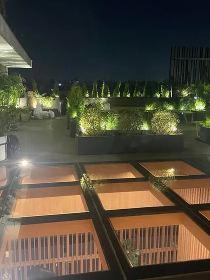 Another view of the same rooftop garden at night. The glass skylights are illuminated from below, casting a warm glow on the terrace and creating a unique architectural feature.