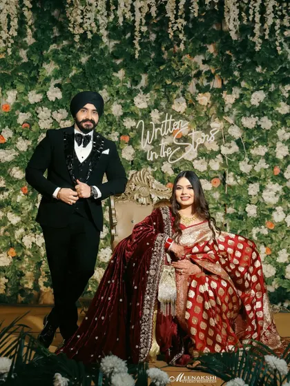 A regal portrait of a couple at their reception, posing in front of a beautiful floral wall with a "Written in the Stars" neon sign. This shot is both grand and personal.