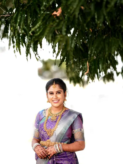 A smiling portrait of the bride-to-be, framed by the leaves of a tree.