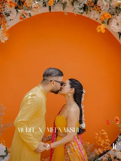 A romantic kiss in front of a stunning floral backdrop at a Haldi ceremony in Thailand.