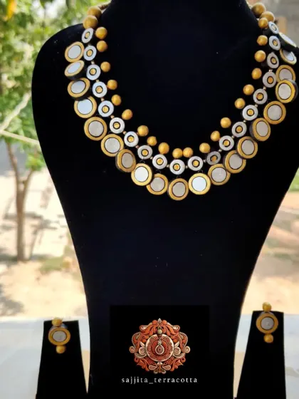 The terracotta coin necklace displayed on a bust, showing how it sits elegantly on the neckline. This helps buyers visualize how the product will look when worn or displayed.