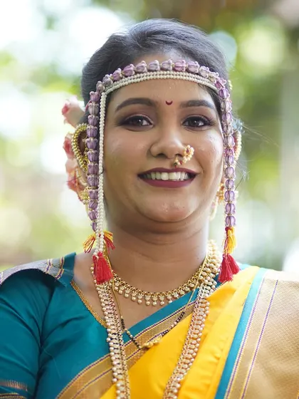 A bright, smiling portrait of the bride. The makeup features a bold lip color that complements her yellow and teal saree beautifully.