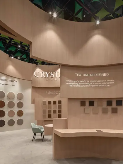 A close-up of the product display area within the Safelam pavilion, where laminate samples are presented on curved walls under focused spotlights. The tagline "Texture Redefined" is integrated into the architecture, reinforcing the brand message.